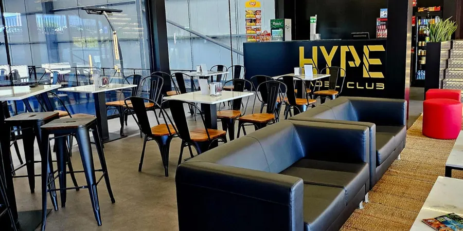 Bar do Hype Padel Club, com o logótipo HYPE dourado no balcão, sofás pretos e mesas brancas.