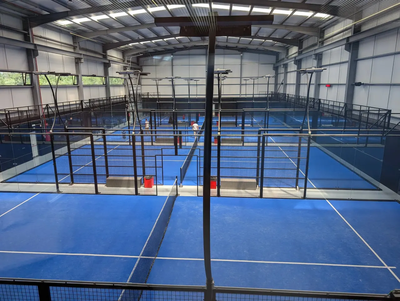 Os quatro campos azuis do Hype Padel Club lado a lado, debaixo da cobertura metálica do pavilhão.