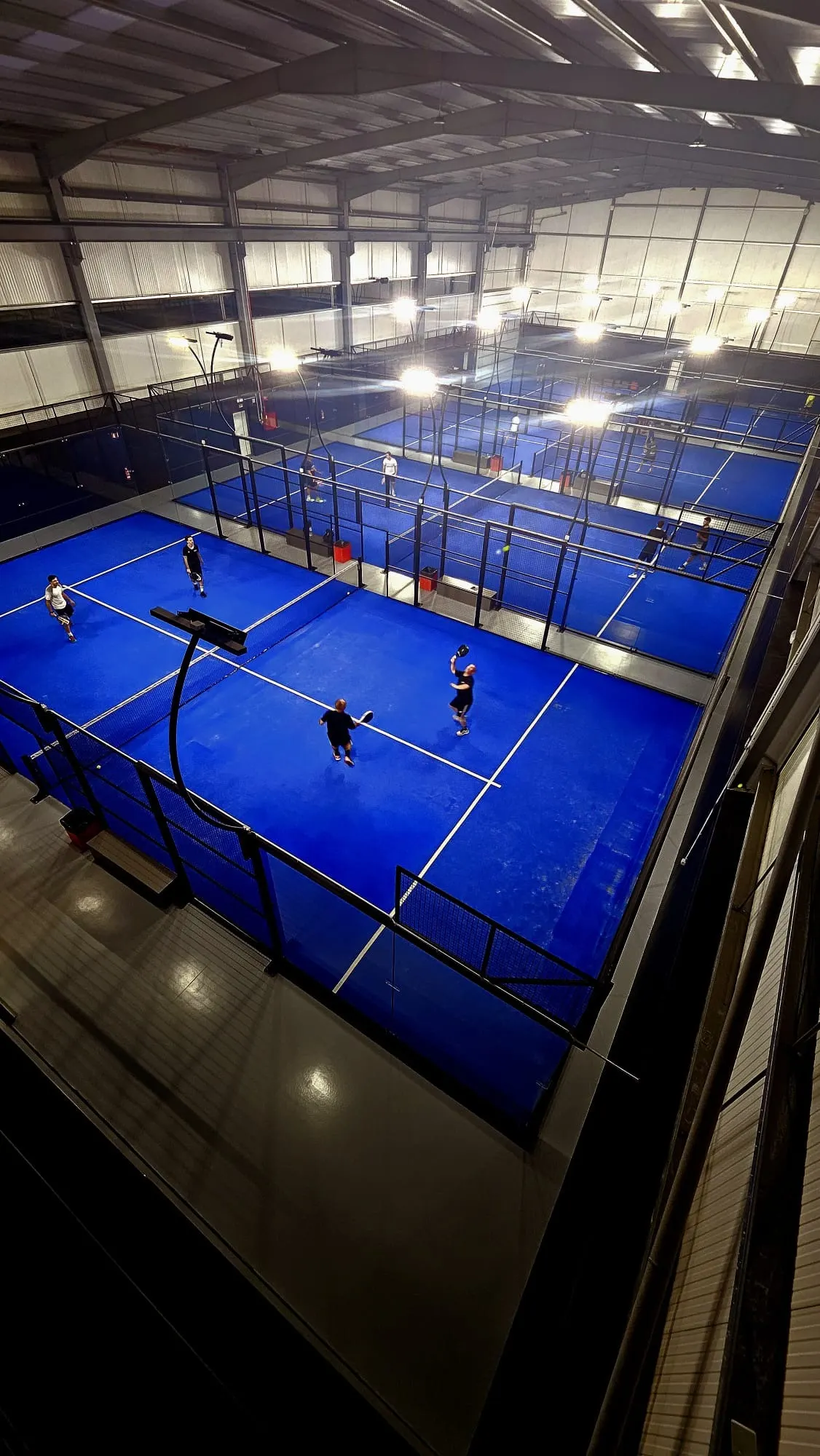 Os campos azuis do Hype Padel Club vistos de cima, à noite, com jogadores a meio de um jogo.