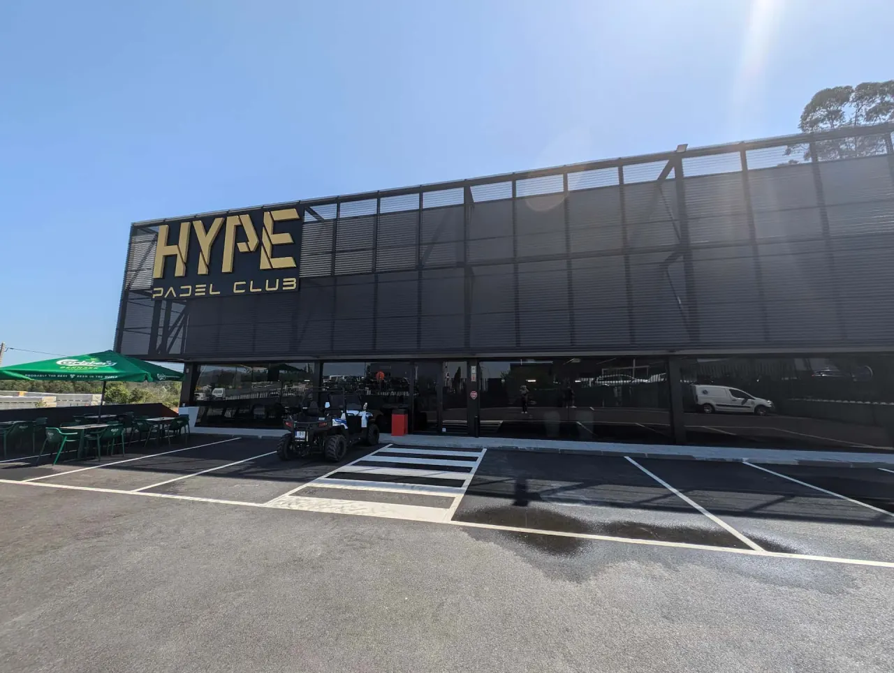 Fachada do Hype Padel Club, em Sendim, com as letras douradas HYPE PADEL CLUB e o parque de estacionamento à frente.
