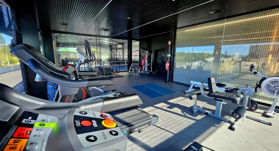Ginásio do Hype Padel Club com passadeira, máquinas de musculação e uma parede de vidro virada para os campos.